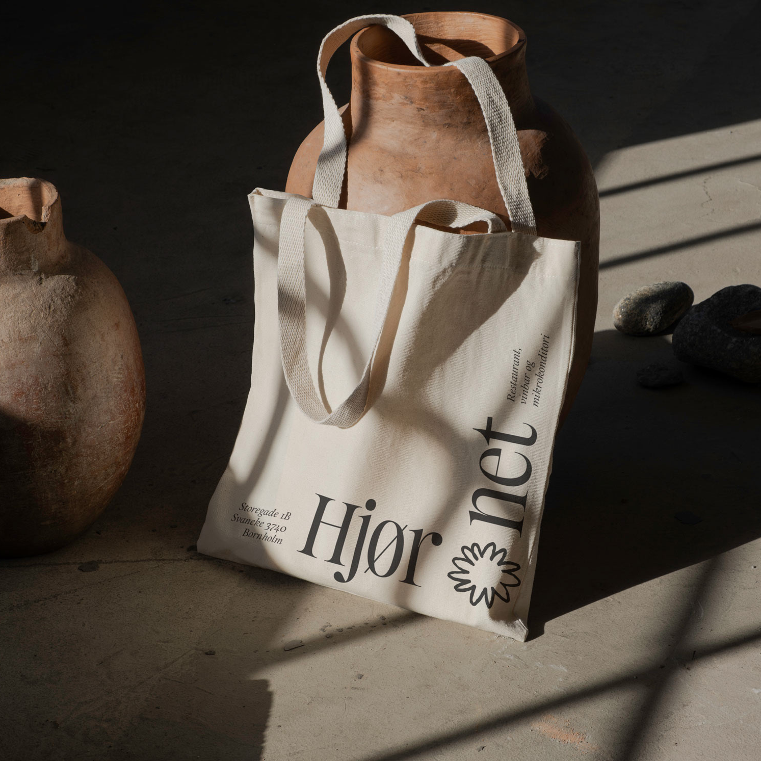 Beige tote bag with 'Hjornet' branding on a dark surface with ceramics